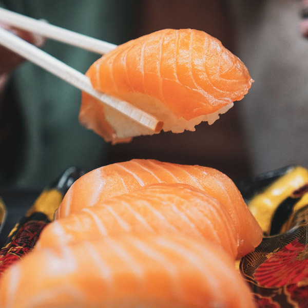 salmon sushi in a row and one is being lifted with chopsticks