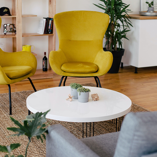 Apartment living room with wood floors, plush yellow wingback chairs, large potted plants, and round white coffee table.